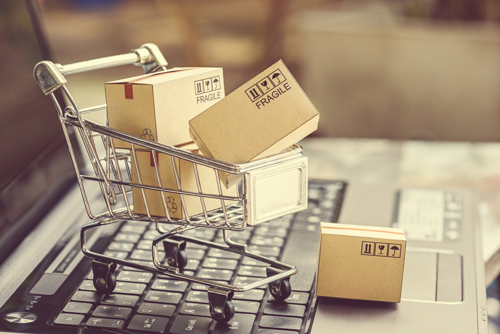 Same day ecommerce courier services by Transol Sameday - miniature shopping cart filled with fragile parcels placed on a laptop keyboard representing online shopping and delivery